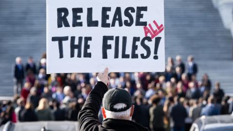 A man holds a sign reading 'Release the files' 