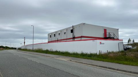 Photograph of the outside of the BCP site. It is a white building with white fencing, and "Kier" can be seen on the side of the site. 