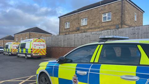 Street with two police vans and a police car on it.