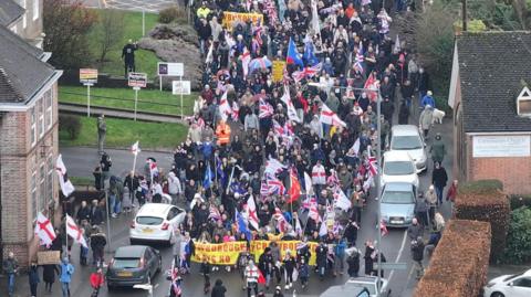 A group of protesters, many with Union Jack flags, marching down a street.