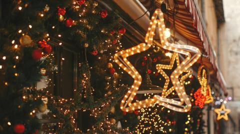 A collection of Christmas lights and wreaths is seen hanging from an awning in festive colours of red, gold and green