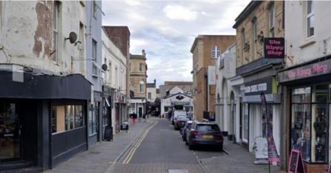 A Google maps street view of West Street in Weston-super-Mare. There are businesses either side of the street and cars parked on one side of the road.