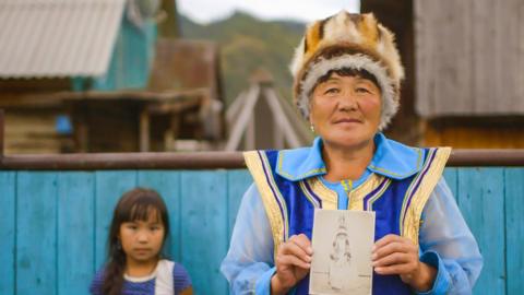 A woman in traditional clothes holding up a photo