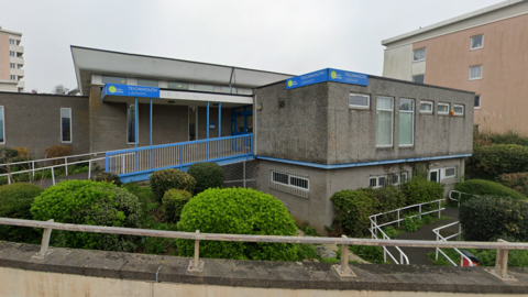 Teignmouth Library with a Teignmouth Library sign written in white on a blue background, there are also blue painted stairs leading to the front door 