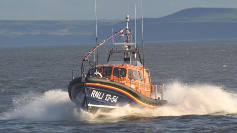 The Shannon class lifeboat which has a blue bottom and orange top. Bunting is displayed at the top of the boat.