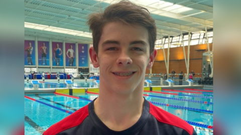 A young man smiles with a swimming pool behind him. 