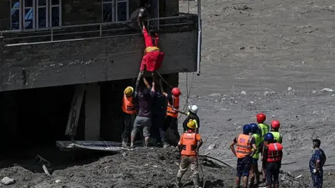 Police personnel rescue stranded residents from houses lying deluged in sludge after flash floods at Trishuli in Nepal's Nuwakot district on August 27, 2026.