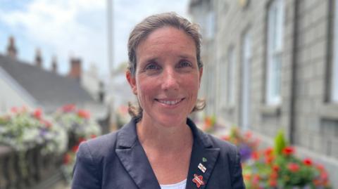 Deputy Lindsay de Sausmarez, who is wearing a suit, smiles at the camera.