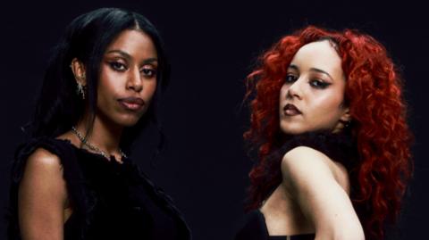 A portrait image of Nova Twins. They are both wearing black clothes