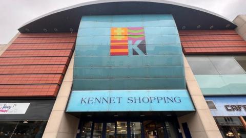 An external picture of the Kennet Shopping centre with a large blue sign, with a cafe nero next to it.
