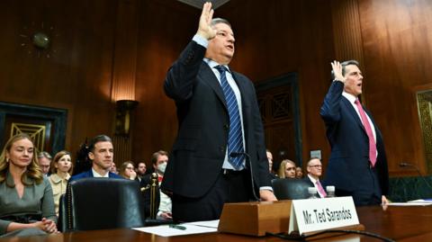 Two men wearing suits raise their right hands as they are sworn in for a Senate hearing in a courtroom