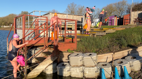 Four people getting in or out of the lake, with people drying themselves off or climbing out of it.