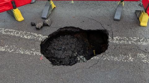 A road with a large, deep, hole in the middle of it