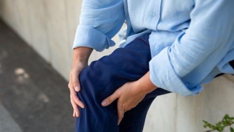 Someone in a light blue shirt and jeans holding the front and back of their knee.