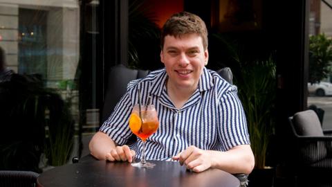 Alex waiting outside a bar with a cocktail