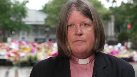 Reverend Marie-Anne Kent in front of floral tributes