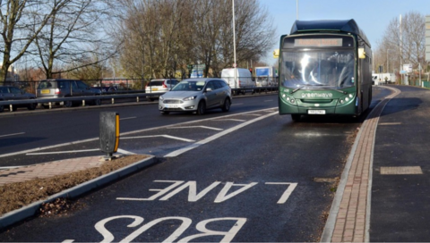 Green Bus driving on bus lane road.