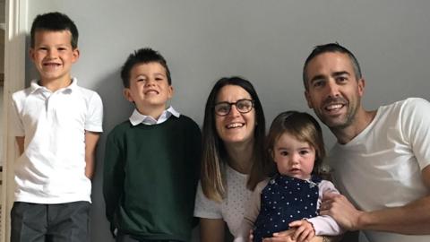 Josh Vickery, his wife and children Arthur, Henry and Elsie pose for a picture by a white wall background. 