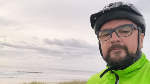 Ian Price wearing a cycle hat, glasses and hi-viz cycling jacket