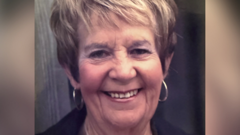 Ms Breed, who has short dark blonde hair and wears hoop earrings, smiles at the camera. 
