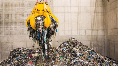 A composite image showing a mechanical claw hovering above a pile of rubbish at a waste incinerator plant.