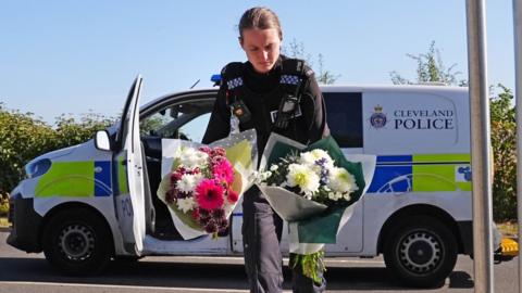 A police officer lays flowers following the crash on the A66.