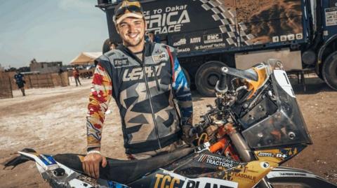 Robbie Wallace with his motorbike and in a sandy area