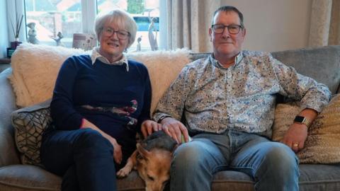 Margaret and Tim Metcalfe sat on a sofa with a dog