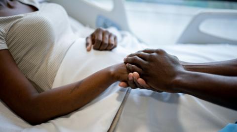 stock image of someone reaching towards a hospital bed and holding the hand of a patient