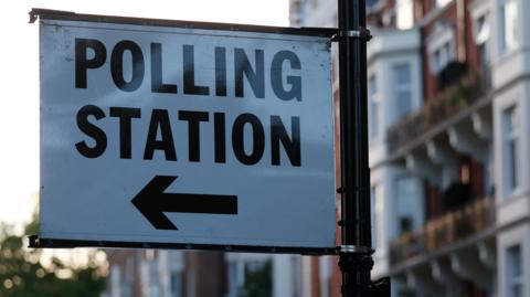 Sign with the words polling station and an arrow attached to a lamp post 