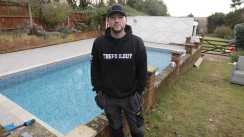 Miles Laflin is stood in front of a swimming pool. He is wearing all black and smiling at the camera.