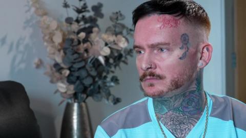 Andrew Dearden, wearing a green T-shirt with a full neck tattoo and an animal tattoo on his temple, speaks to the BBC