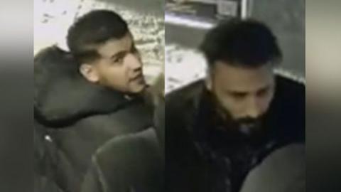 A CCTV image composite showing two men. The one of the left has short dark hair and stubble and is wearing a black puffer jacket with a hood. He is looking over his right shoulder. The man on the right has dark hair, cropped at the sides, and a black beard. He is looking down and is wearing dark clothing