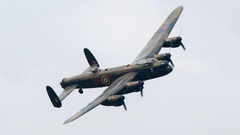 A Lancaster bomber flying in a grey sky.