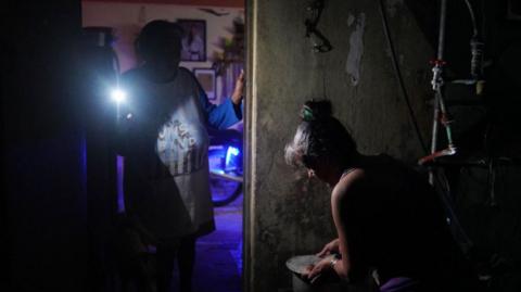 A woman boils water while another lights her with a mobile phone during a nationwide blackout caused by a grid failure in Matanzas, Cuba, on October 18, 2024.