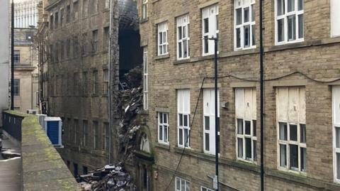 A multi-storey building with a large hole in the side and rubble hanging out. 