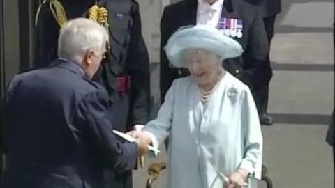 Queen Elizabeth the Queen Mother accepting a piece of paper during a parade.