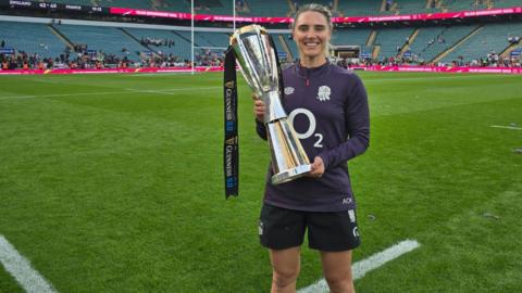 Aimee Ellen O'Keeffe standing at Twickenham holding a rugby trophy which the Red Roses had won