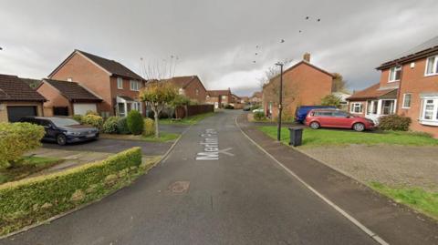 A screengrab taken from Google Maps showing Merlin Park in Portishead. The Image shows a residential street with detached houses, hedges and several cars parked in driveways.