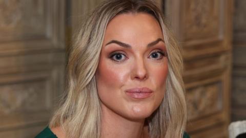 A close-up of Rachel. She has long blonde hair and is wearing a green top.