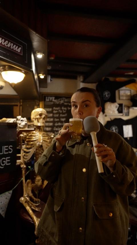 Harriet fisher in a pub with a microphine drinking a small beer