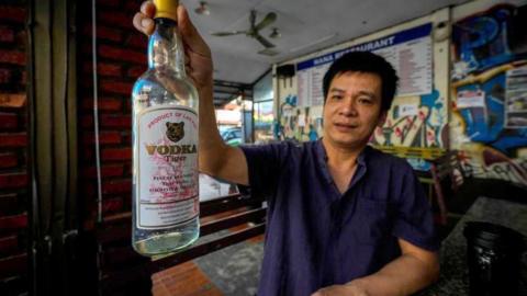 Duong Duc Toan, the manager of Nana Backpack hostel in Vang Vieng, holds a bottle of Tiger vodka in the hostel's bar