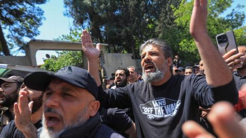 A crowd of Druze men gesture with their hands in the air