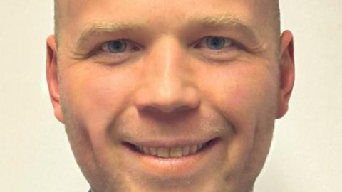 Hugo Wils, who has a shaved head, smiles for the camera.