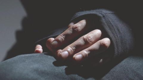 A close-up picture of some hands, folded in someone's lap. The person is wearing a long-sleeved black top and the sleeves are covering the back of their hands. 
