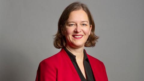 Fleur Anderson looking at camera. She is wearing a red blazer and a black blouse. 