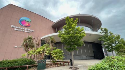 A college building with a rounded entrance and trees in front of it. There is signage on the side of the building which identifies it as Cheshire College South and West.