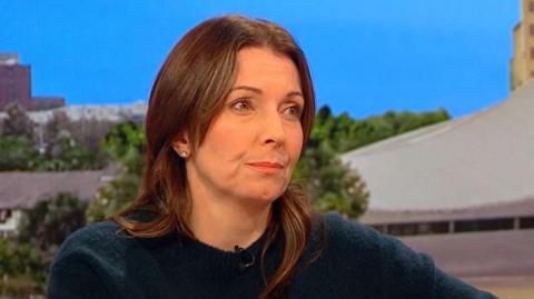 Polly sits in the BBC Breakfast studio, she has long brown hair and wears a dark blue jumper