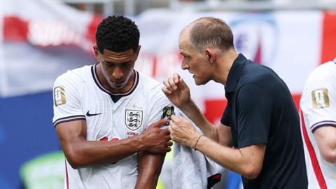 Jude Bellingham of England holds his shoulder as he speaks with Thomas Tuchel, Manager of England.