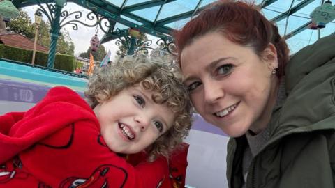 Boy with curly hair and red pullover with woman in green coat.